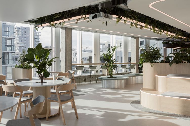 Spacious office lounge with natural lighting, featuring wooden tables and chairs