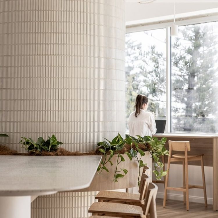 Interior space featuring a textured white tiled pillar next to a minimalist wooden table and chairs
