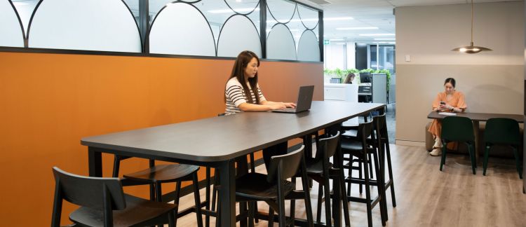 A staff member working on a computer while sitting on a black stool in an office setting