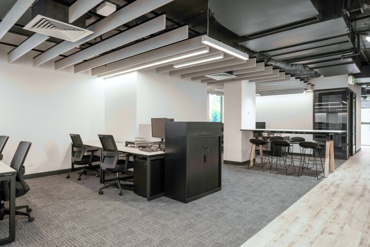 A communal table with stools is set against a glass-partitioned room, while exposed ceiling ductwork adds an industrial touch.