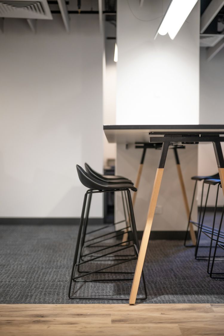 A modern space with a table flanked by black tall stools, lit by a ceiling light from above.