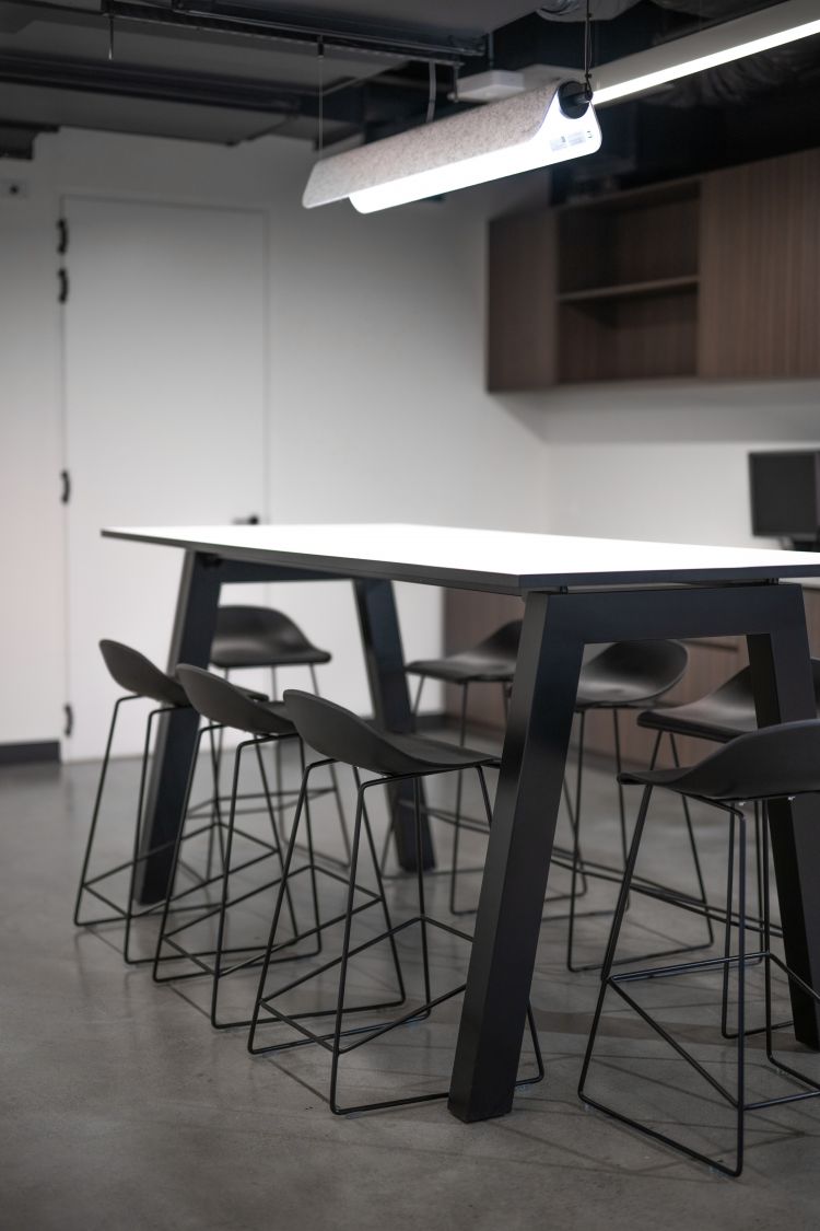 A contemporary setting featuring a table accompanied by black high stools, illuminated by an overhead ceiling light.