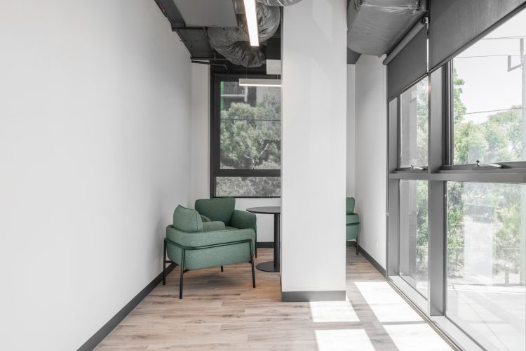 Three lounge chairs and a black table in the corner of a modern building next to big windows