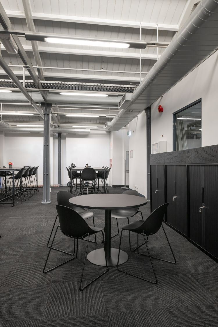 Modern industrial-style office space with exposed ceiling beams, fluorescent lighting, and air ducts.