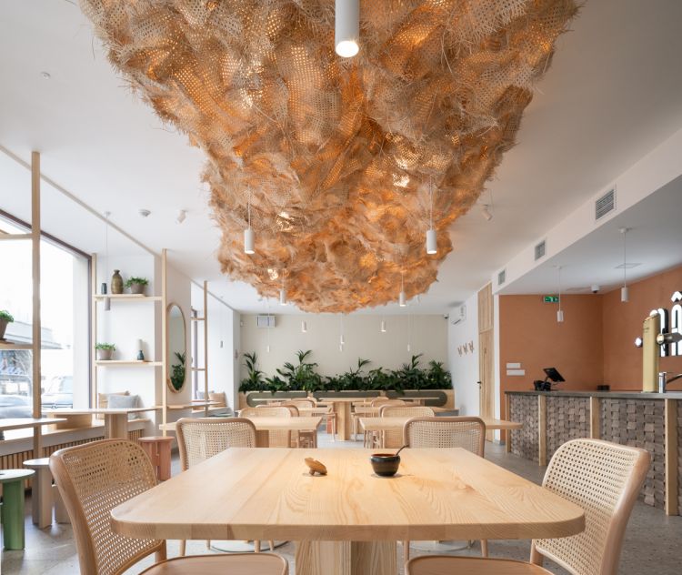 Close-up of a bistro's interior highlighting a textured rattan cloud canopy from which cylindrical pendant lights hang.