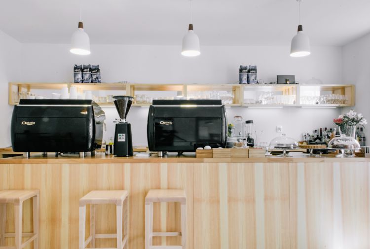 The café counter features sleek black espresso machines flanked by coffee accessories and a coffee grinder
