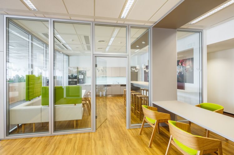 A modern office interior featuring glass partitions revealing bright green chairs and white furniture.