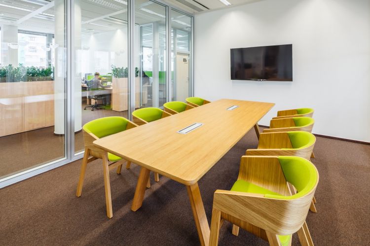 A contemporary office meeting room with a long wooden table surrounded by vibrant green cushioned chairs with wooden frames.