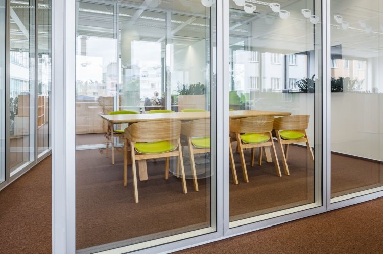 A modern office meeting room with floor-to-ceiling glass walls, offering a transparent view into the space.