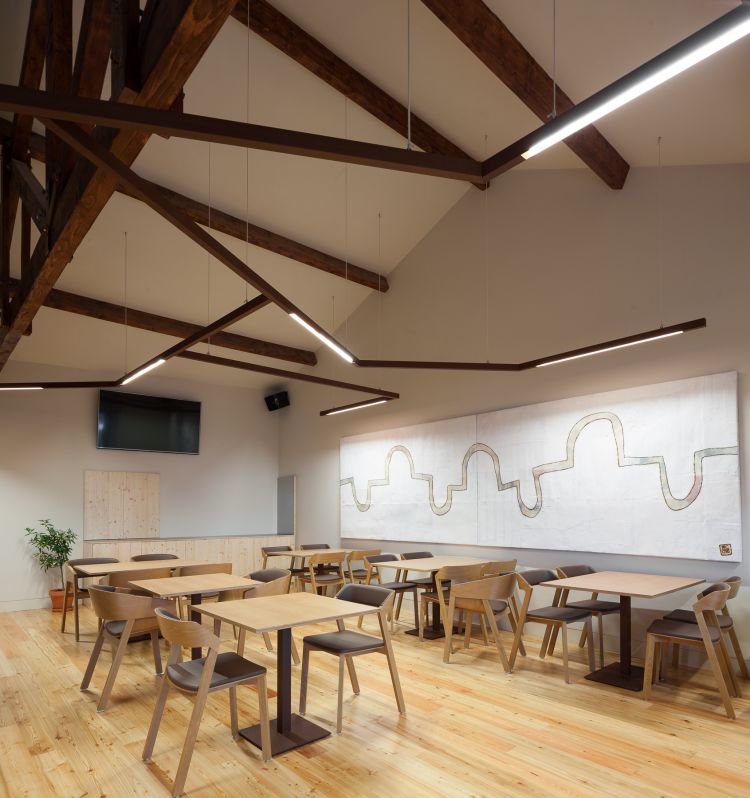 The space features multiple wooden tables paired with rounded chairs on a light wooden floor.