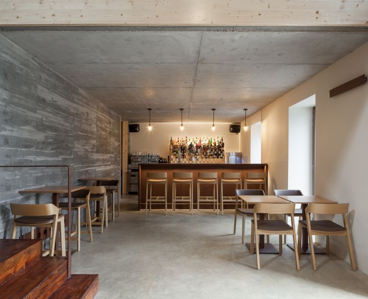 The space features a blend of modern and rustic elements, with an exposed concrete ceiling, dining chairs and table and a modern counter bar.