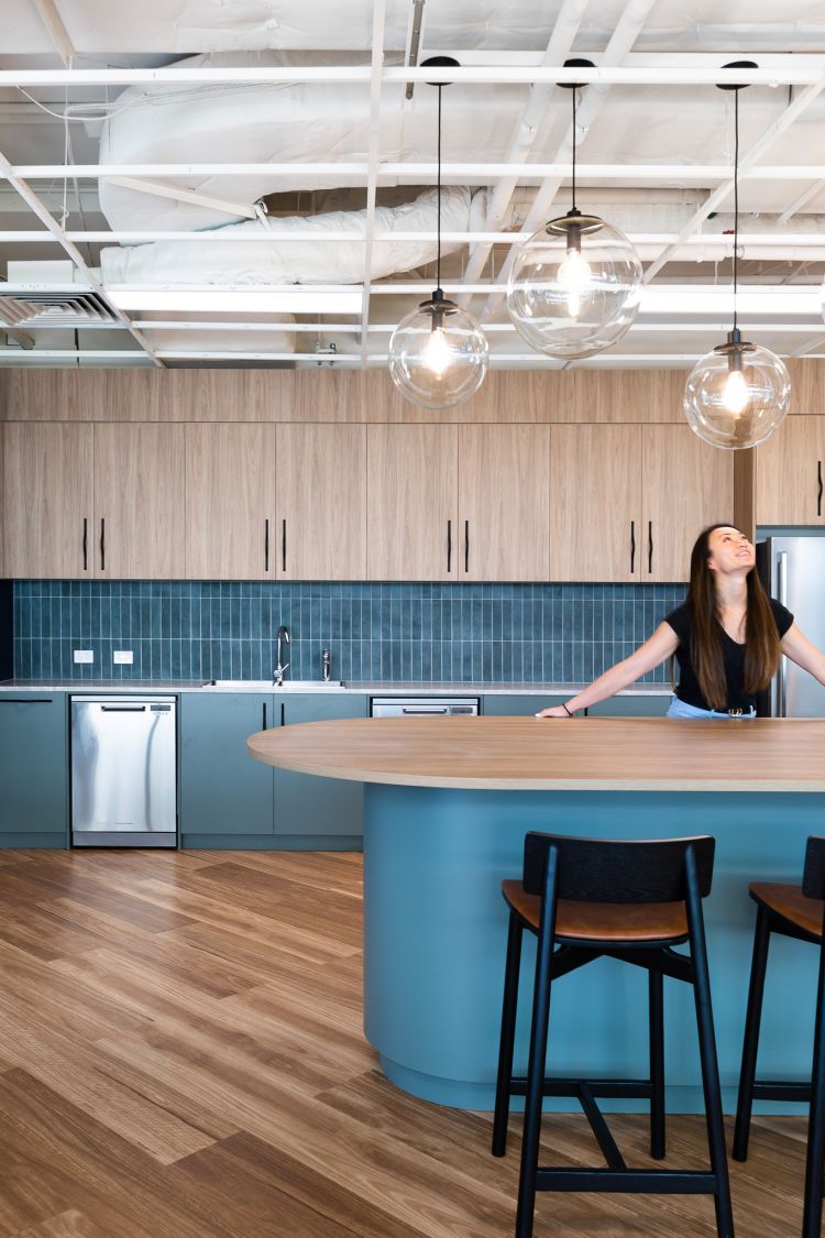 Modern kitchen area in an office setting with a blend of wooden and blue cabinetry.