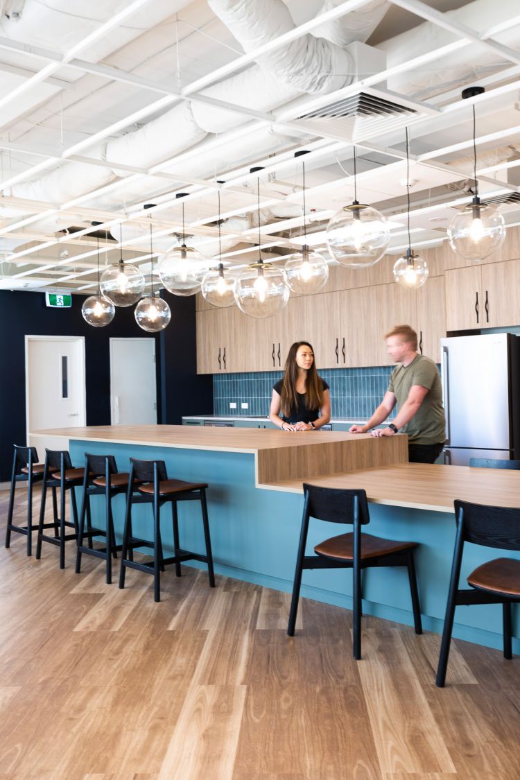 Contemporary kitchen space in an office featuring wooden cabinetry, a blue-tiled backsplash, and a wooden-topped blue island. 