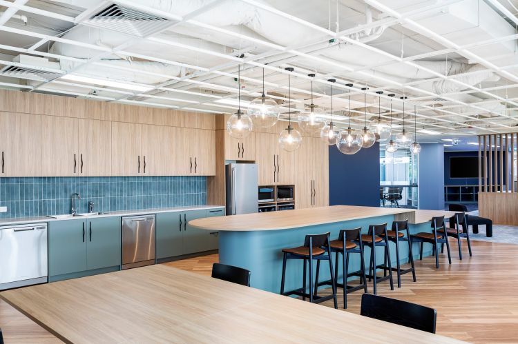 Modern office kitchen and breakout area featuring sleek wooden cabinetry, a blue countertop, and a complementing blue-tiled backsplash.