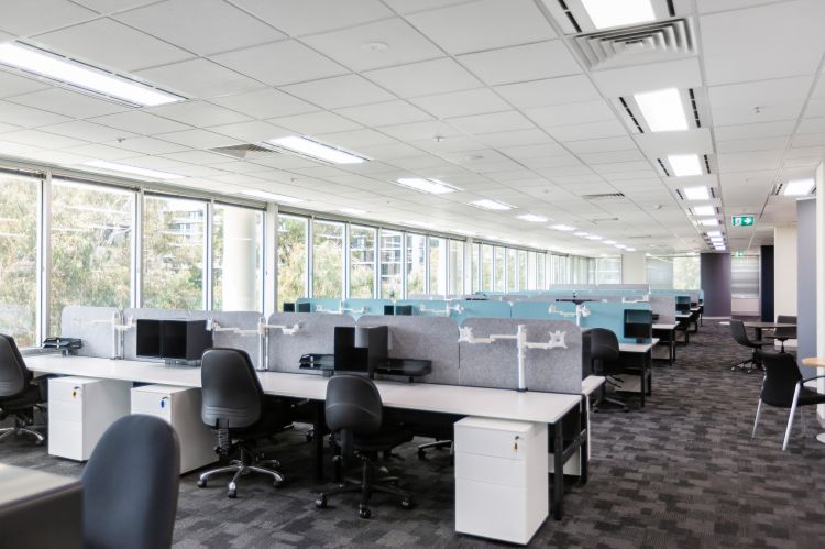 Spacious office interior with rows of white desks equipped with modern computer monitors and ergonomic black chairs.