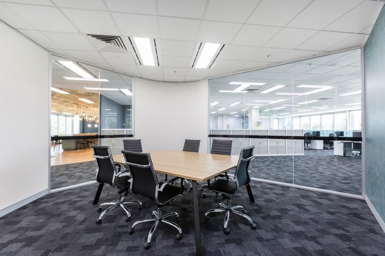 Modern office meeting area featuring a rectangular wooden table surrounded by four sleek black leather chairs with chrome details. 