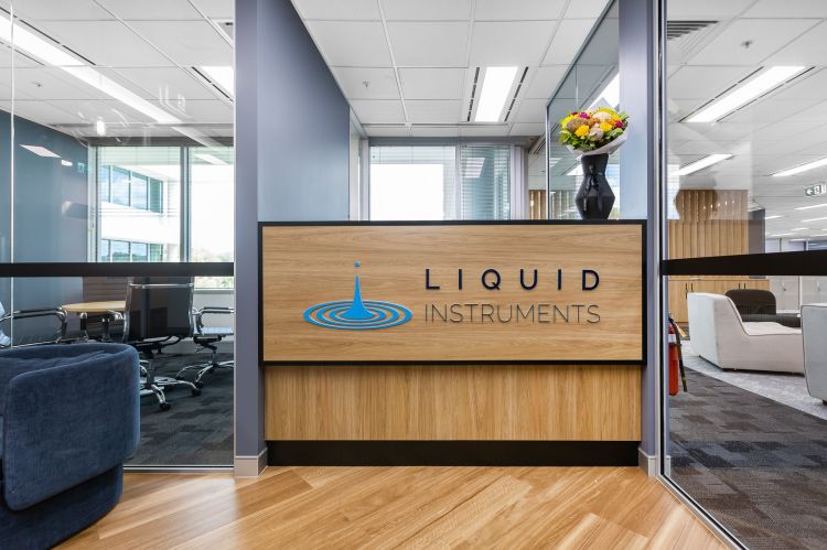 Modern office interior featuring a wooden reception desk with the logo and name "LIQUID INSTRUMENTS" prominently displayed.