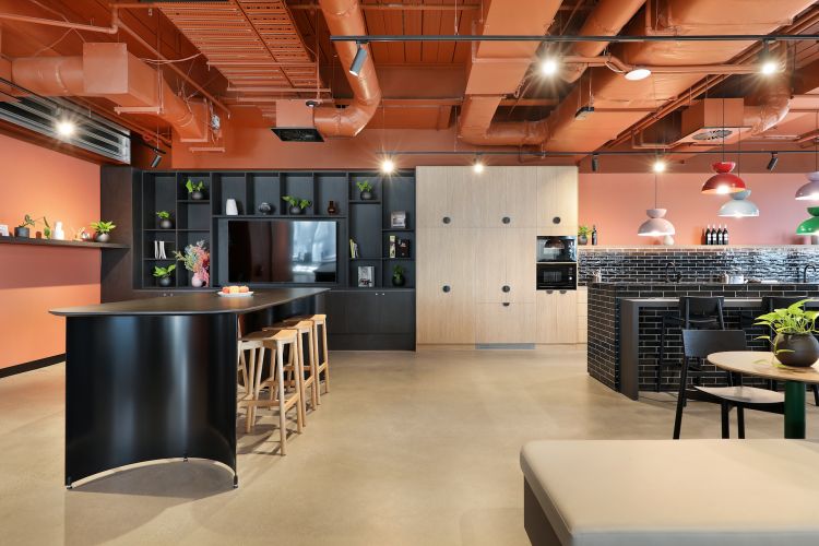 Contemporary office kitchen area with orange walls, prominent terracotta-colored exposed ductwork overhead, sleek black and wooden cabinetry