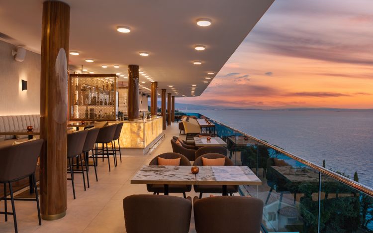 Elegant indoor bar and dining area with wooden pillars, marble tables, and sleek barstools, all illuminated by soft ceiling lights.