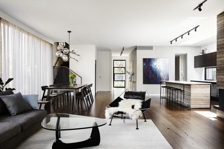 Modern living space with wooden flooring, a sleek dining area with black chairs, a distinctive overhead glass bulb light fixture, and sheer window curtains.