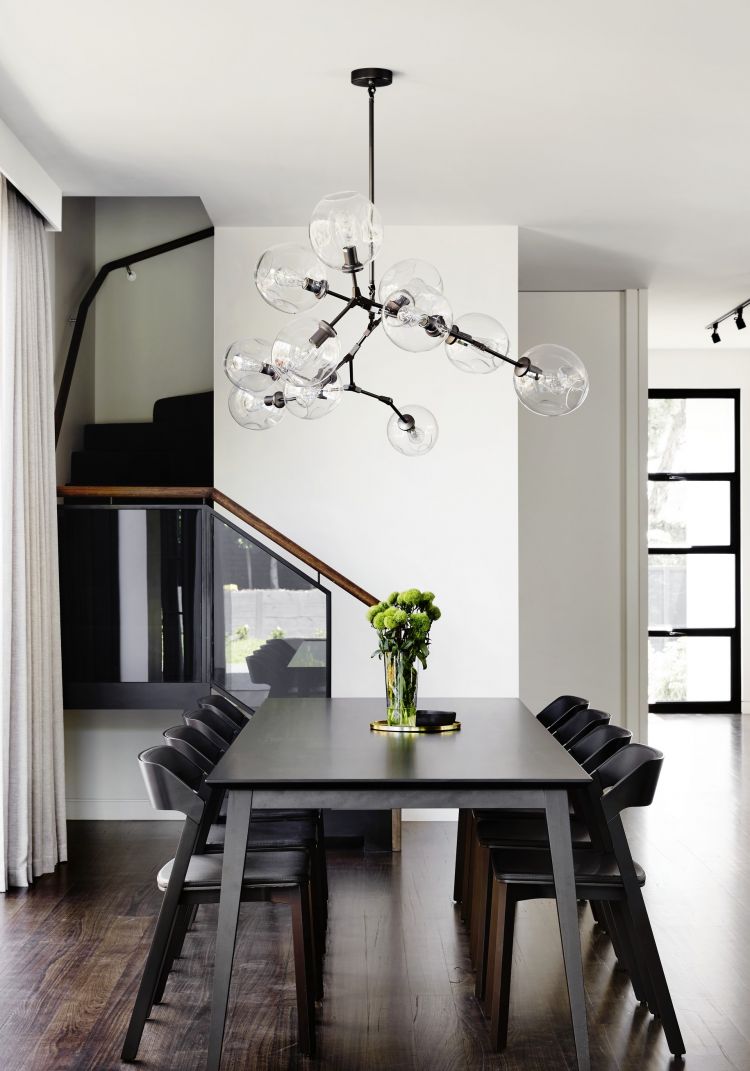 Minimalist dining area with a dark wooden table, black chairs aligned neatly, and a striking glass bulb chandelier overhead.