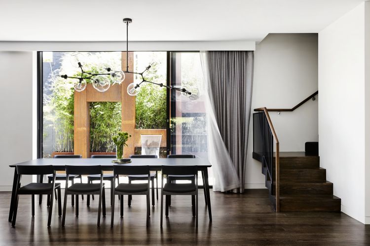 Contemporary dining area with a sleek black table and matching chairs set beneath a unique pendant light featuring multiple clear bulbs