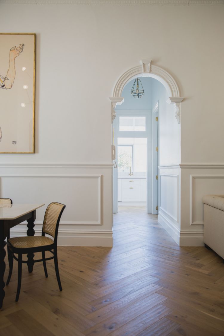 Spacious interior of a refined room featuring a detailed archway that leads to a light blue corridor with a window at the end. 