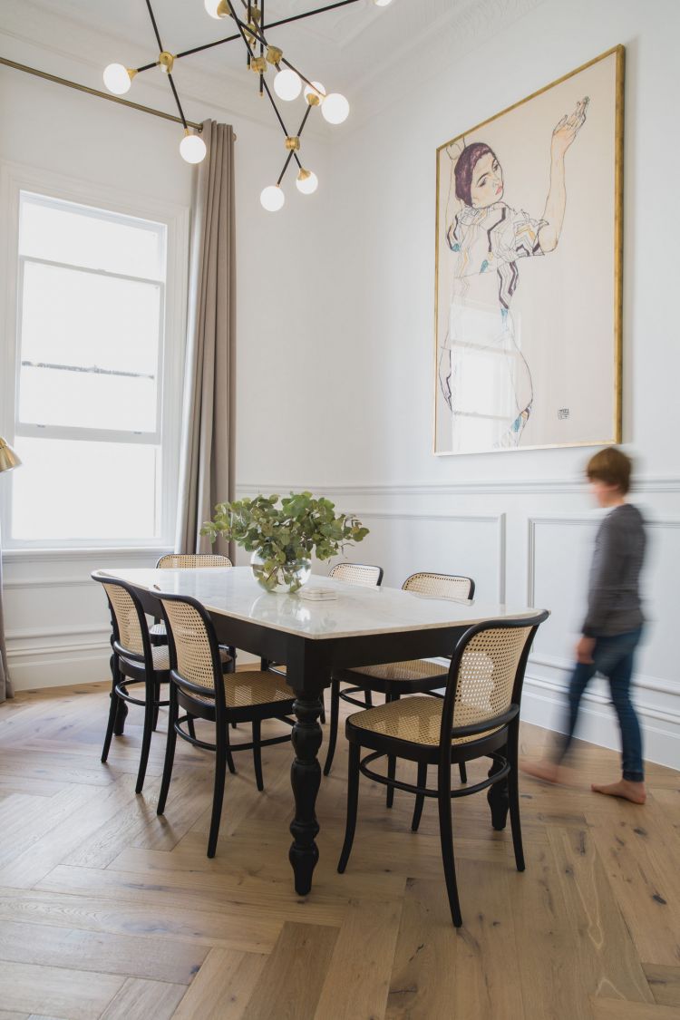 Spacious and well-lit dining room featuring a white marble table surrounded by black chairs with woven seat patterns.