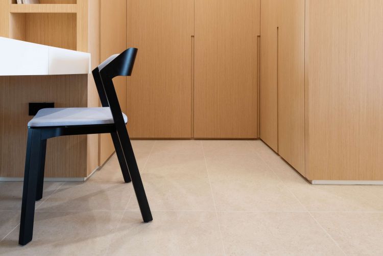 Close-up view of a modern kitchen featuring a sleek black chair with a light gray cushion next to light wooden cabinetry and a beige-tiled floor