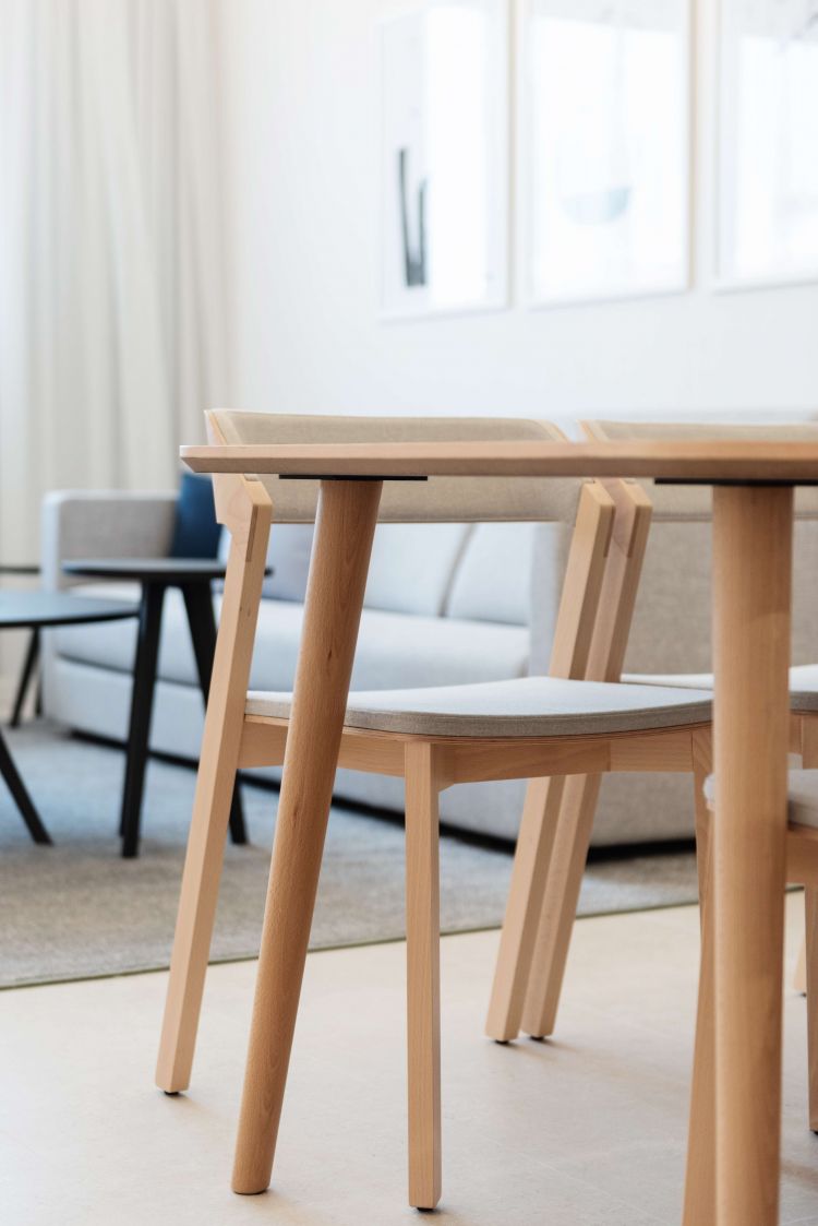 Detail shot of a light wooden dining table and chairs with beige cushions in a bright living area