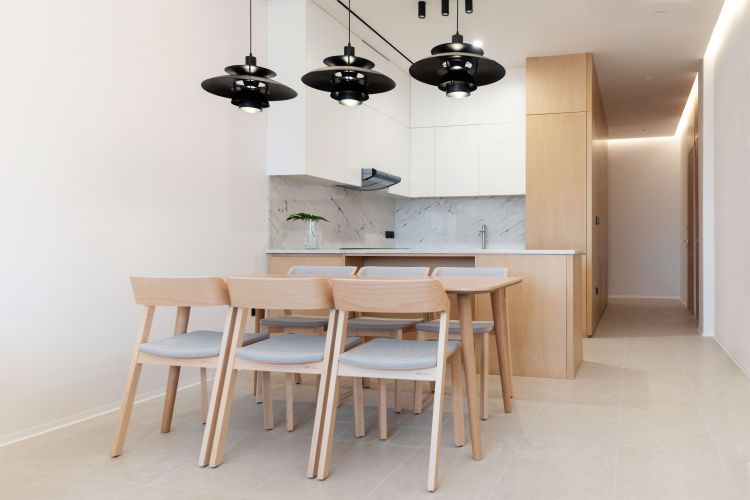 Modern kitchen and dining area featuring a light wooden dining set with beige cushions and black pendant lights overhead