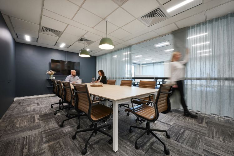 A contemporary meeting room featuring a long wooden table surrounded by leather chairs