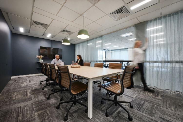 A contemporary meeting room featuring a long wooden table surrounded by leather chairs