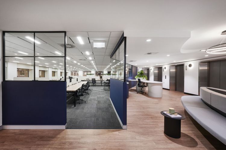 Modern and spacious office interior with clear glass partitions revealing rows of desks and chairs.