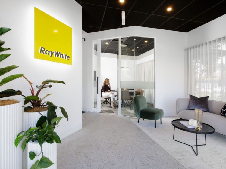 Modern office interior with a vibrant yellow 'Ray White' logo on a white wall.