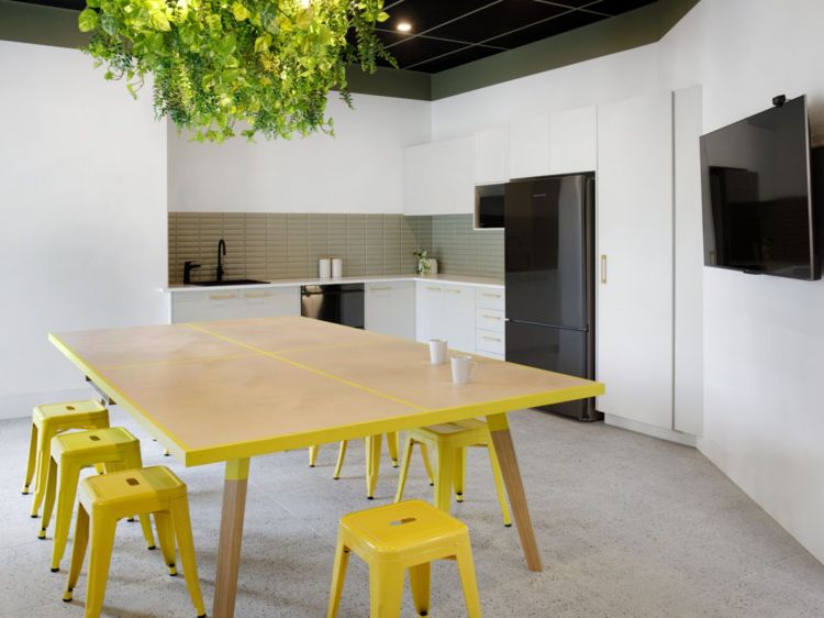 Contemporary kitchenette and dining area with a striking yellow-accented wooden table surrounded by matching yellow stools.