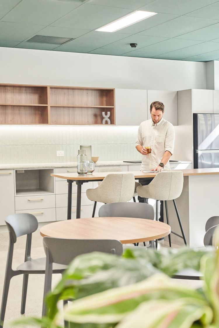 A kitchen counter in a modern office with chairs, a round table, and wooden shelving