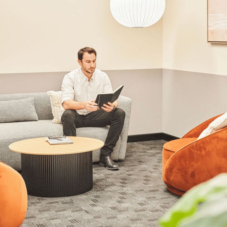 The room features a round wooden coffee table, an orange armchair, a large hanging white spherical lamp, and a framed abstract artwork on the wall