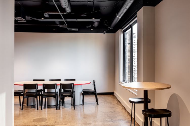 A minimalist conference room with a modern design, featuring a white and red round table surrounded by black  Andi chairs