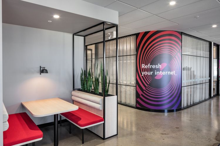 A modern office space featuring a small seating area with a wooden table, red cushioned benches, and a wall-mounted lamp