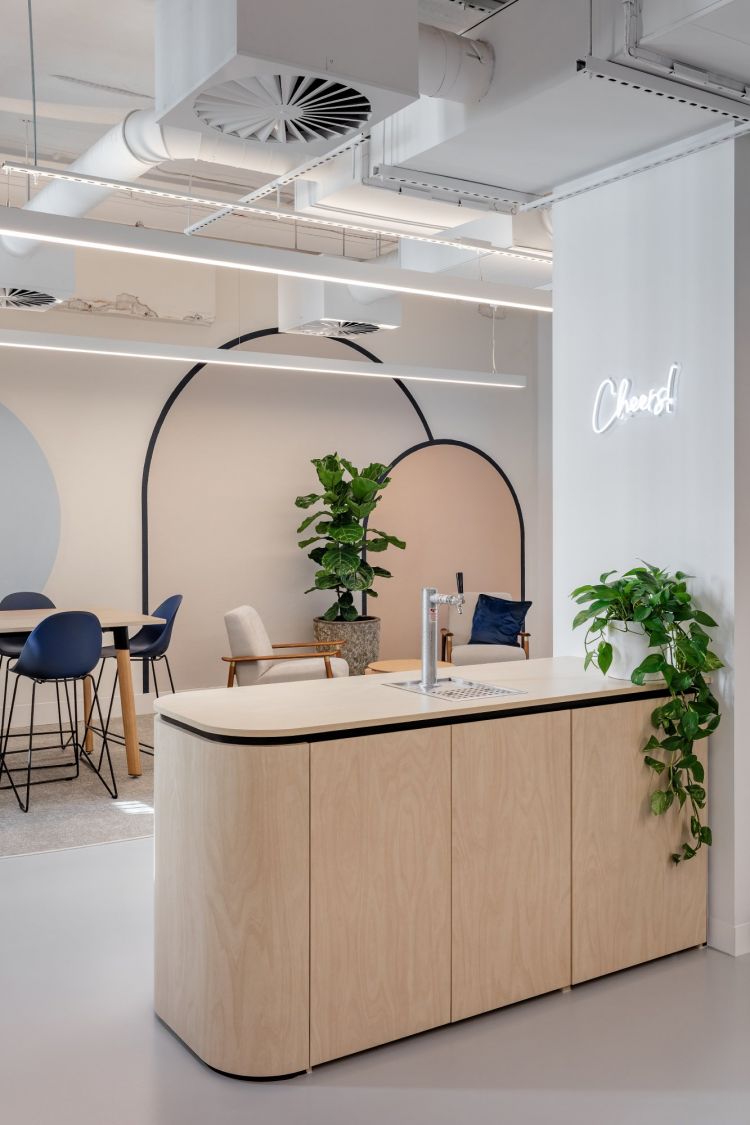 A modern office reception area featuring a curvilinear wooden desk with a built-in tap, against a backdrop of large, circular wall designs.