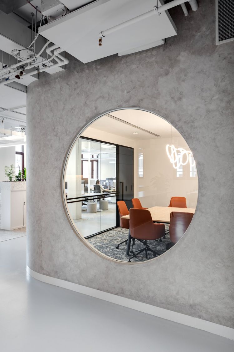 A large, round mirror on a textured grey wall in an office, reflecting an interior space.