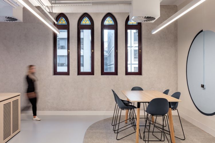 A bright office space featuring a meeting area with a wooden table and black Pebble stools