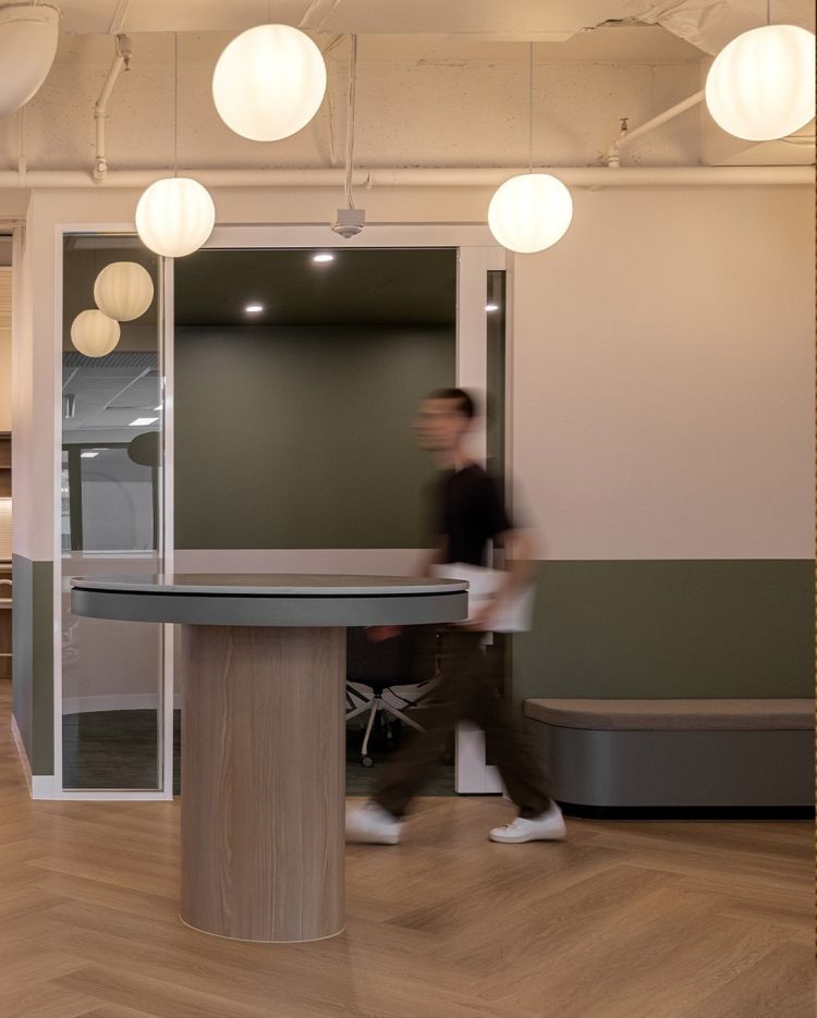 An office interior featuring a high table with a circular top and wooden base, positioned near a glass partition