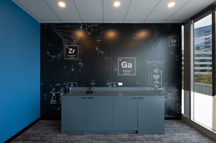 An office corner with a large wall graphic featuring a periodic table and scientific illustrations.