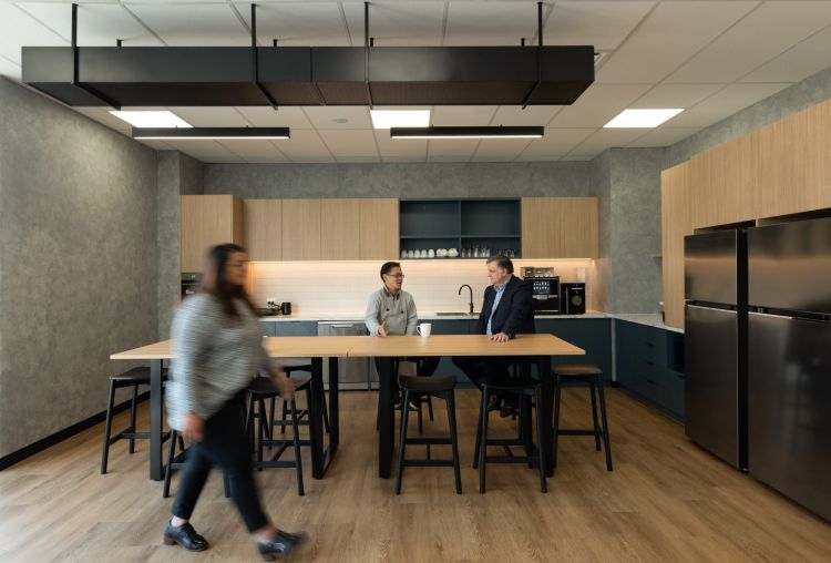 An office kitchen with people chatting at a high table, modern appliances, and minimalist design.