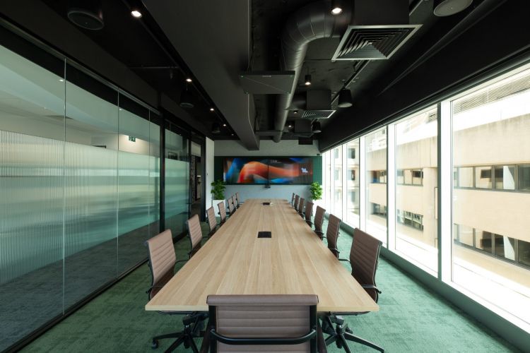 A modern conference room with a long wooden table, chairs, and large windows providing a city view, plus a colorful wall art piece at the end.