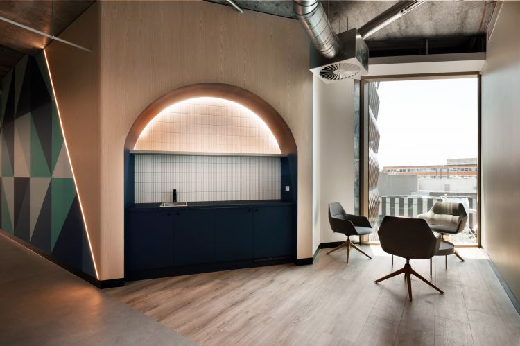 A modern office nook with a blue cabinet and sink, wooden walls, and a large arched lighting feature. 