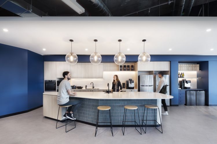 A modern office kitchen with a curved island, Hugo bar stools, white subway tile backsplash, and large globe pendant lights.