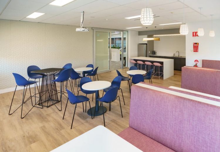 Bright and modern office breakout area featuring round tables with Pebble blue chairs and textured white walls